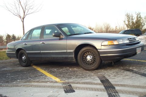 2001 Ford Crown Victoria - This sedan has a dark gray exterior and black steel wheels, parked in a lot with visible tire marks.