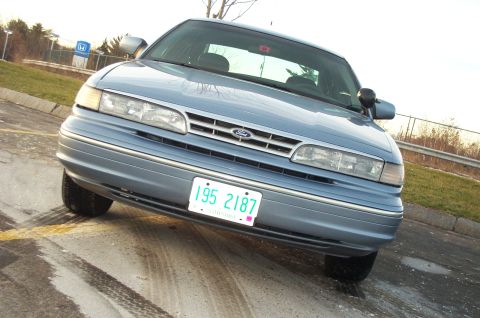 2001 Ford Crown Victoria - A blue 2001 Ford Crown Victoria is viewed from the front, parked on a wet surface with tire tracks visible.