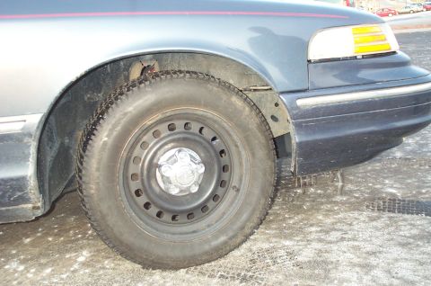2001 Ford Crown Victoria - The front quarter panel and wheel of a dark-colored 2001 Ford Crown Victoria are visible in this close-up shot.