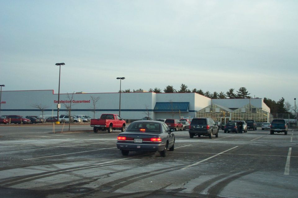 Parking lot with various cars and a large retail building under a cloudy sky