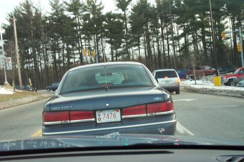 2001 Ford Crown Victoria - A dark blue 2001 Ford Crown Victoria is seen from behind on a road with other vehicles and trees.