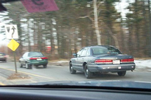 2001 Ford Crown Victoria - A dark blue 2001 Ford Crown Victoria is seen from behind on a road, with another car ahead.