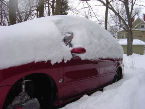 1998 Ford Taurus - A red car is almost completely covered by a thick layer of snow, with only its side visible.
