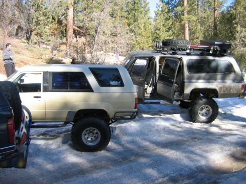1985 Ford Bronco - Two off-road SUVs are parked in a snowy landscape, with one vehicle's doors open.