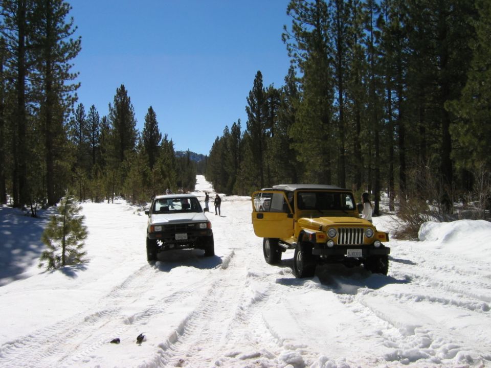 White SUV and lifted yellow Jeep on snowy forest road