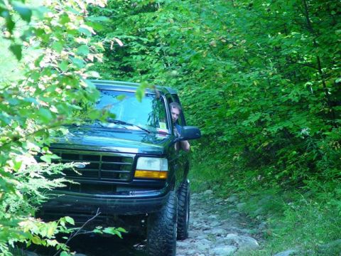 1996 Ford Bronco - 1996 Ford Bronco navigates a rough, tree-lined path.