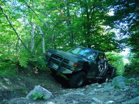 1996 Ford Bronco - A Ford F-Series truck maneuvers through a challenging off-road course surrounded by dense foliage.