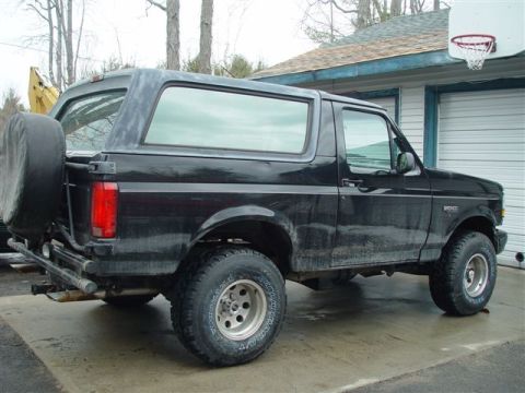 1996 Ford Bronco - This black 1996 Ford Bronco is viewed from the rear quarter, showing its external spare tire mount and classic SUV body style.