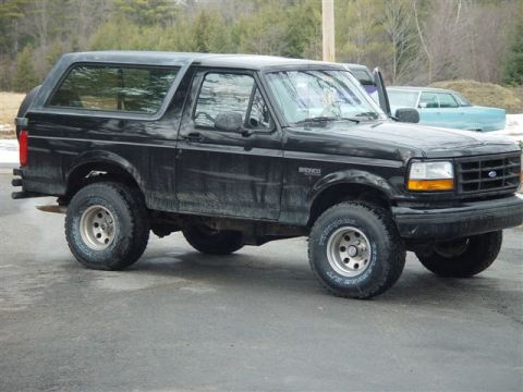 1996 Ford Bronco - A black Ford Bronco is parked outside on a paved surface with trees and snow in the background.