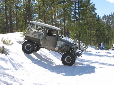 1985 Ford Bronco - Custom off-road vehicle navigates a snow-covered trail in a wooded area.