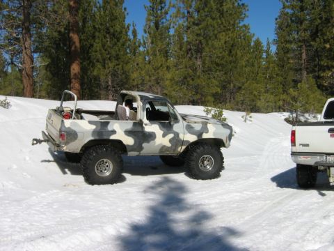 1985 Ford Bronco - A camouflaged pickup truck with a roll bar sits in the snow next to another vehicle.