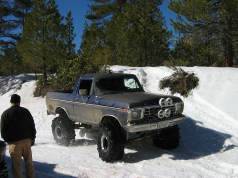 1985 Ford Bronco - Modified Ford Bronco with oversized tires navigates a snowy terrain.
