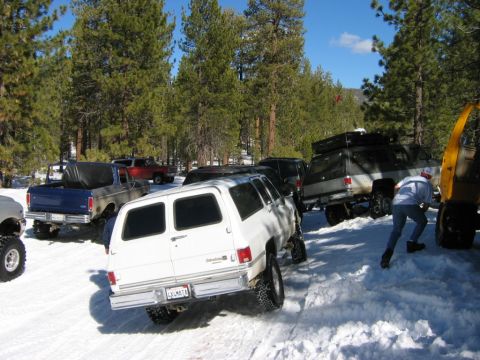 1985 Ford Bronco - A group of off-road vehicles are navigating a snowy, wooded terrain with some assistance.