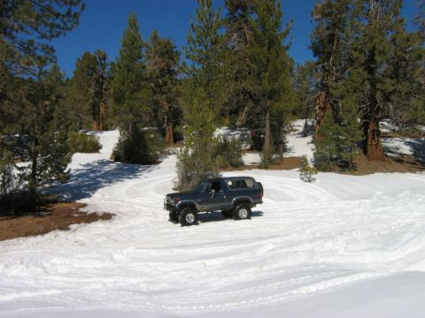 1985 Ford Bronco - A dark blue 1985 Ford Bronco navigates a snowy landscape under a clear blue sky.