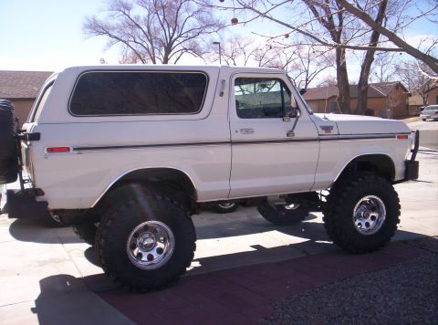 1979 Ford Bronco - White Ford Bronco with lifted suspension and spare tire on the back, parked outdoors.