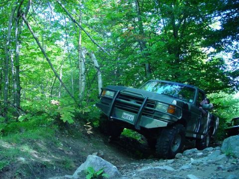 1996 Ford Bronco - A Ford F-Series truck navigates a rocky, wooded trail with another vehicle visible behind it.