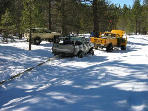 1985 Ford Bronco - Multiple trucks are stuck in the snow, with one being towed out.