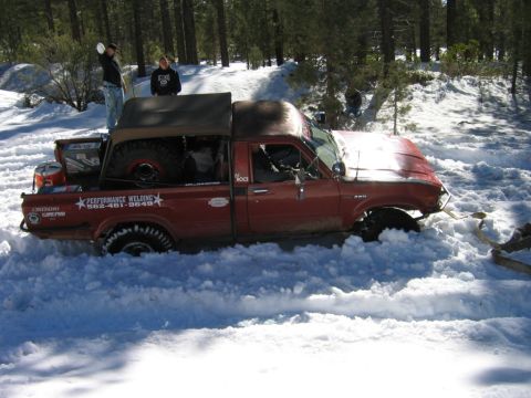 1985 Ford Bronco - A red pickup truck is stuck in the snow with people standing around it.