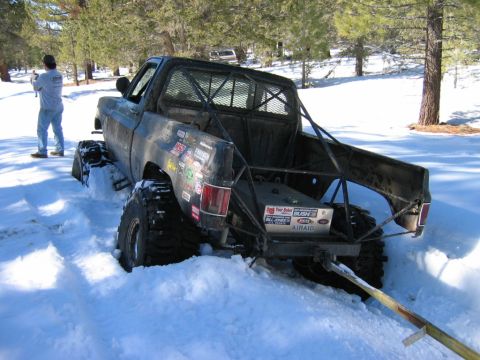 1985 Ford Bronco - Off-road pickup truck with custom roll cage is stuck in deep snow, with another vehicle in the distance.