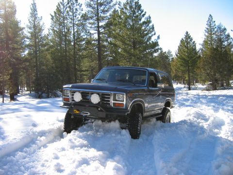 1985 Ford Bronco - SUV with off-road modifications navigates a snowy terrain.