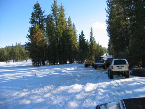 1985 Ford Bronco - A convoy of SUVs navigates a snowy mountain road, with the lead vehicle seen from the rear.