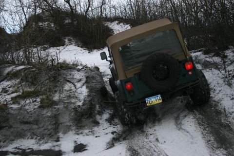 2003 Jeep TJ - A Jeep TJ navigates a challenging snowy and muddy incline, its off-road capability.
