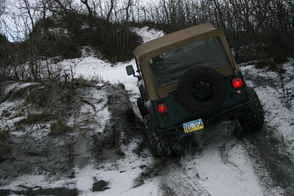 Green Jeep TJ driving up a snowy, muddy trail. License plate reads EEG 954