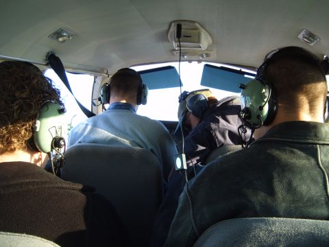 1988 Ford Bronco - Four passengers are seen inside an aircraft cabin, all wearing communication headsets.