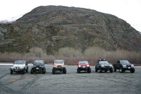 2003 Jeep TJ - A group of off-road vehicles are parked on a gravel lot with a large mountain behind them.