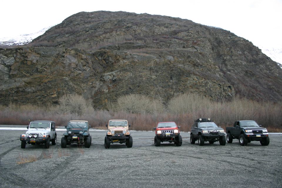 Six modified SUVs and trucks parked in a line on a gravel lot with a mountain in the background