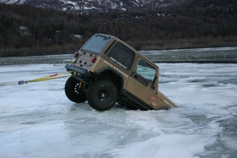 2003 Jeep TJ - A Jeep TJ is partially submerged in ice, with a tow strap attached to its rear, indicating it is stuck.