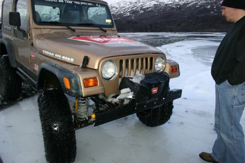 2003 Jeep TJ - A man stands next to a gold Jeep TJ parked on a frozen body of water, with snow-covered mountains in the background.