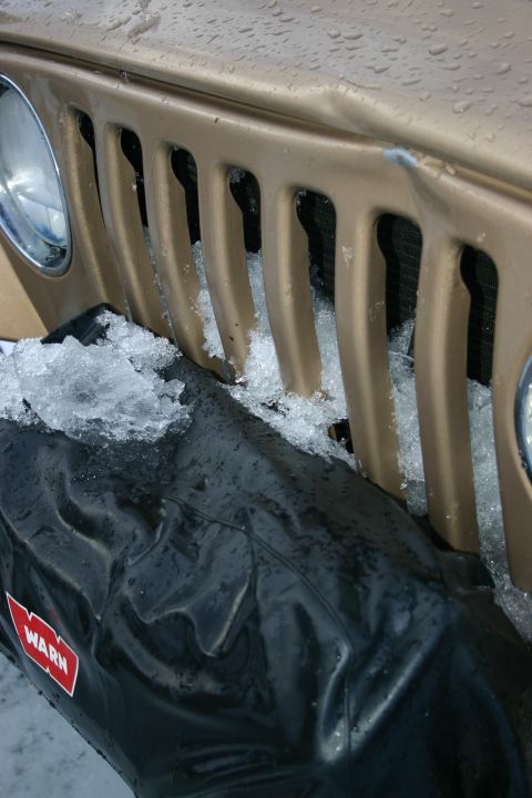 2003 Jeep TJ - Front view of a 2003 Jeep TJ grille covered in snow, with a WARN winch cover visible.