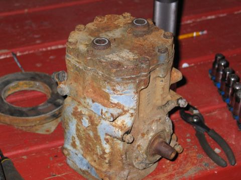 1989 Ford F-150 - A heavily rusted air conditioning compressor sits on a red surface next to a gasket and some tools.
