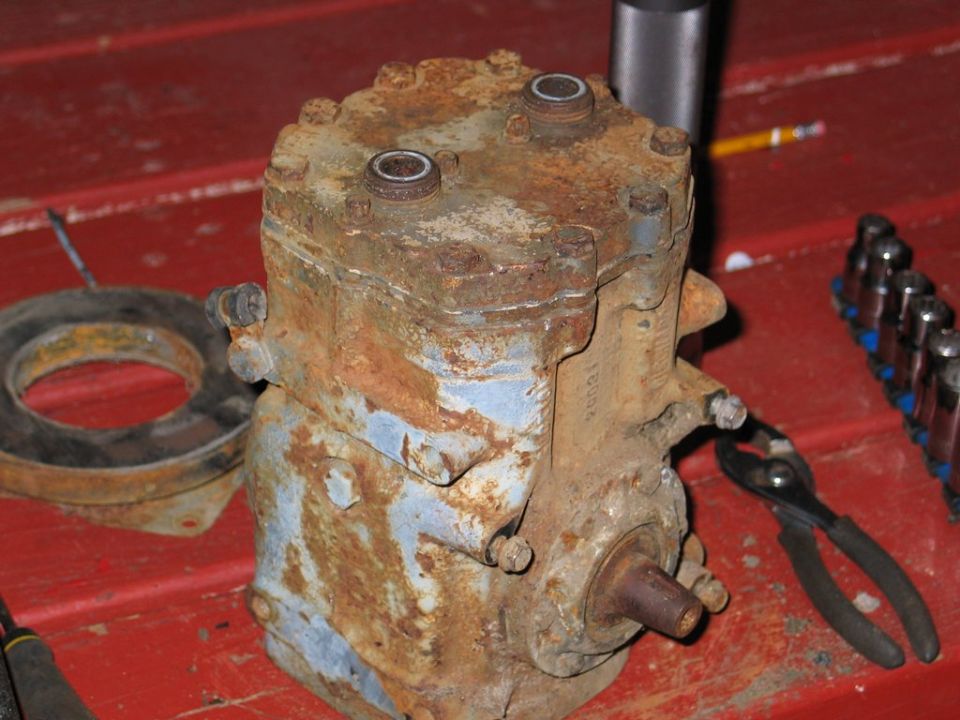 Rusty air conditioning compressor with a gasket and tools on a red surface
