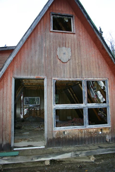 2003 Jeep TJ - Exterior view of a dilapidated wooden cabin with shattered windows and an open doorway.