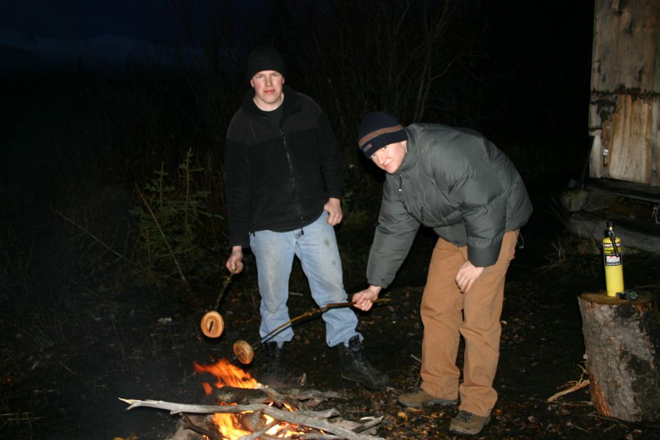 Two men cooking sausages over a campfire at night