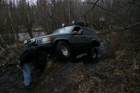 2003 Jeep TJ - A dark 1993 Jeep Grand Cherokee navigates a muddy trail with assistance from a person outside the vehicle.