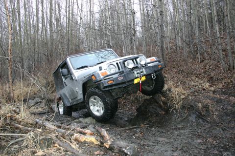 2003 Jeep TJ - Silver Jeep TJ off-roading on a challenging muddy trail through a wooded area.