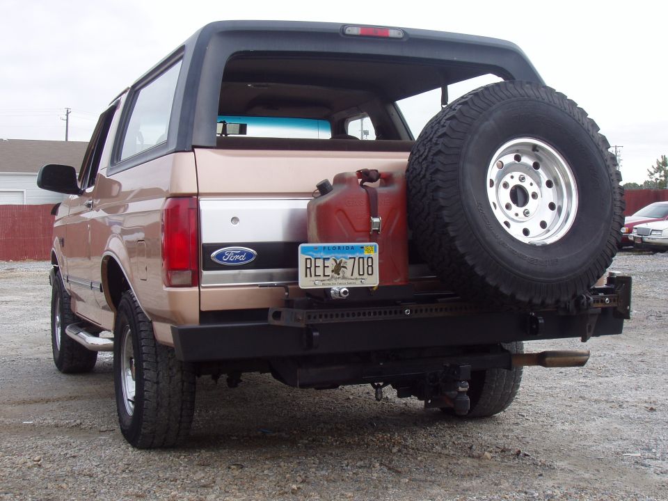 Rear of tan Ford Bronco SUV with spare tire, gas can, and Florida plate on gravel lot.
