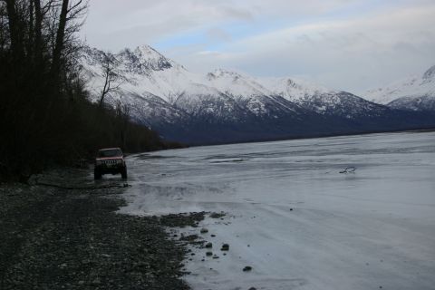 2003 Jeep TJ - A red Jeep TJ drives along a rocky shore next to an icy plain with snow-covered mountains in the background.