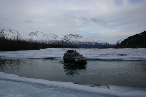 2003 Jeep TJ - SUV navigates icy water with snow-capped mountains in the distance.