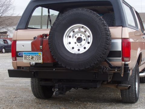 1994 Ford Bronco - The rear of a tan Ford Bronco shows a spare tire mounted externally, a red jerrycan, and a custom bumper with a trailer hitch.