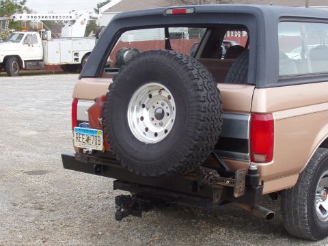 1994 Ford Bronco - Rear view of a tan 1994 Ford Bronco, a spare tire on the tailgate and a custom bumper with a tow hitch.