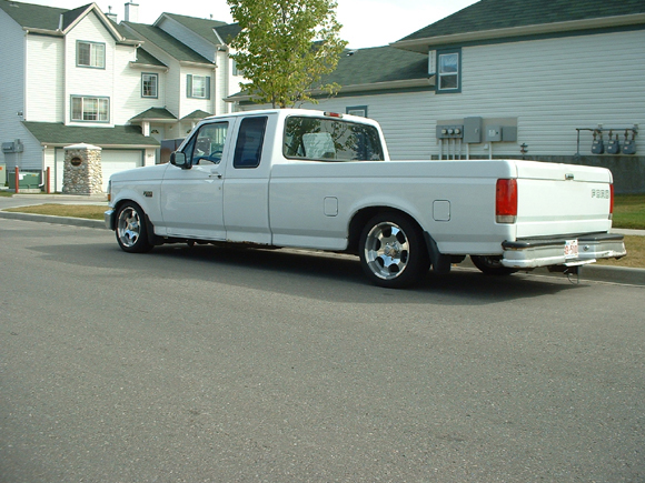 Rear three-quarter of a lowered white Ford F-150 extended cab parked on a residential street