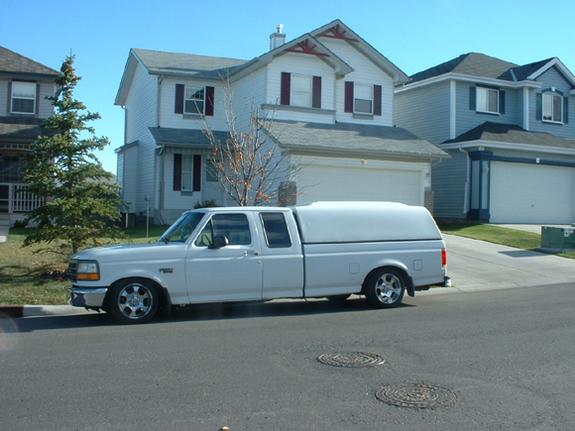 White Ford extended-cab pickup with camper shell lowered in street