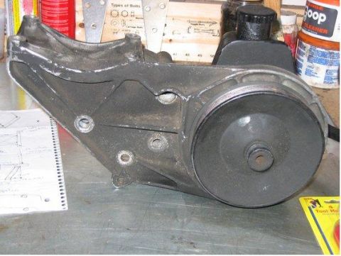 1988 Ford Bronco - A power steering pump bracket assembly sits on a workbench next to a notebook with diagrams.