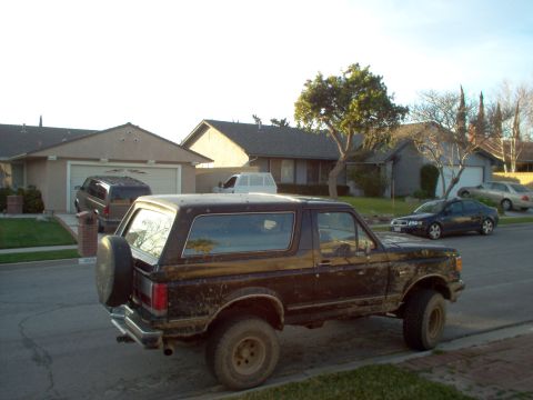 1988 Ford Bronco - Dirty brown Ford Bronco parked curbside on a residential street.
