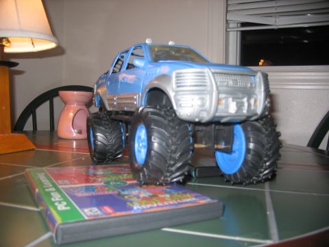 1978 Ford Bronco - A blue toy monster truck with oversized tires sits on a table next to a PC game case.
