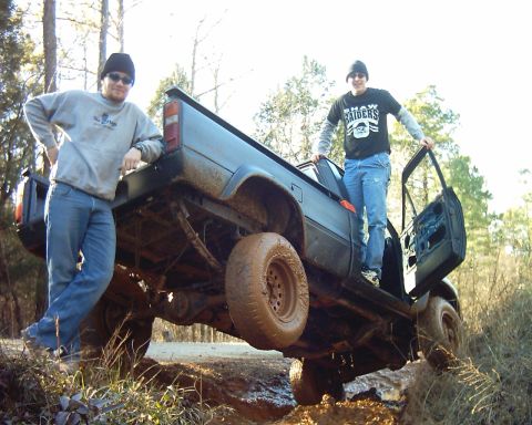 1993 Ford Bronco - Two men stand next to a muddy pickup truck that appears to be stuck in the dirt.